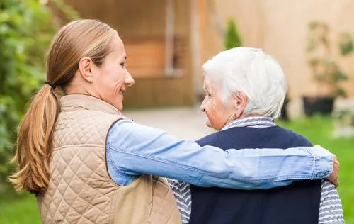 Caregiver walking outdoors with her arm around an older woman