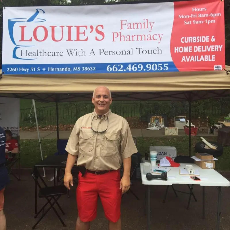 Louie standing in front of the Louie's Family Pharmacy banner at a community event booth in Hernando